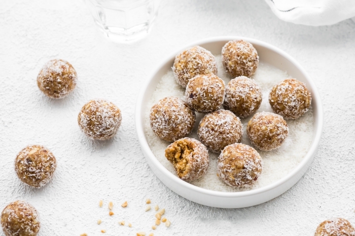 white table, peanut butter bites, covered with coconut flakes, energy bites recipe, nuts scattered around