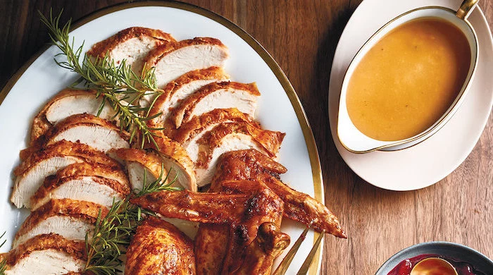 gravy in a jug, how to cook a turkey in the oven, turkey slices, fresh rosemary, in a white plate, wooden table