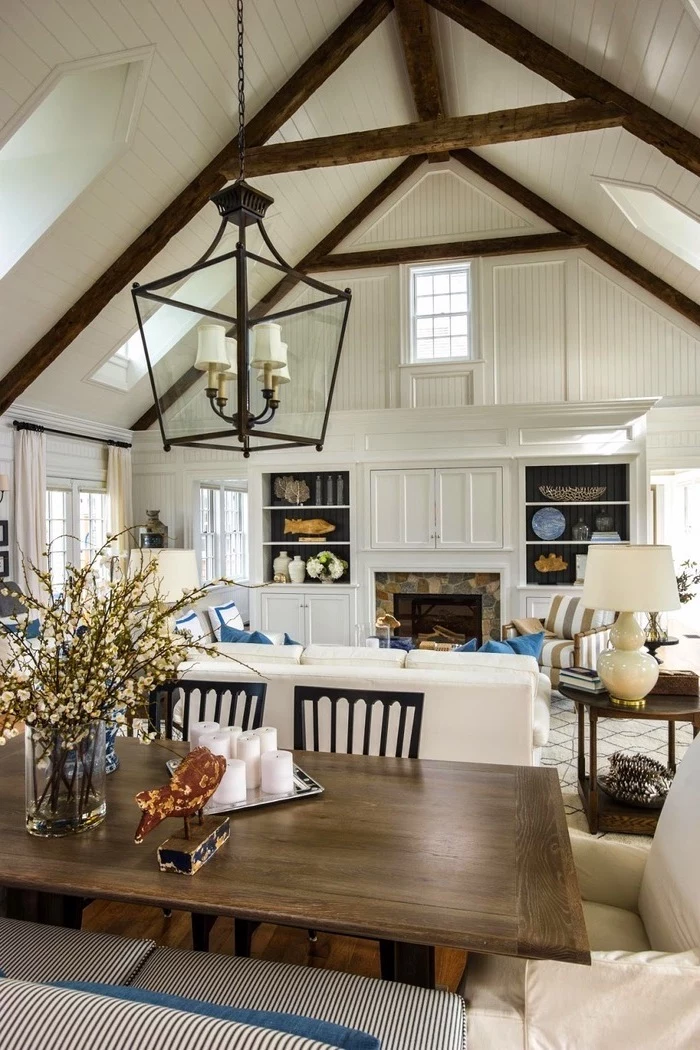 wooden dining table, white sofa, blue throw pillows, vaulted ceiling with beams, ceiling with skylights