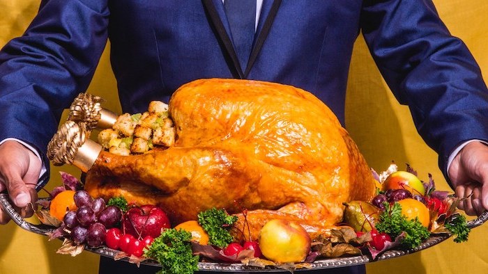 how to prepare a turkey, man in a blue suit, carrying a silver tray, wit stuffed turkey, fruits and herbs on the side
