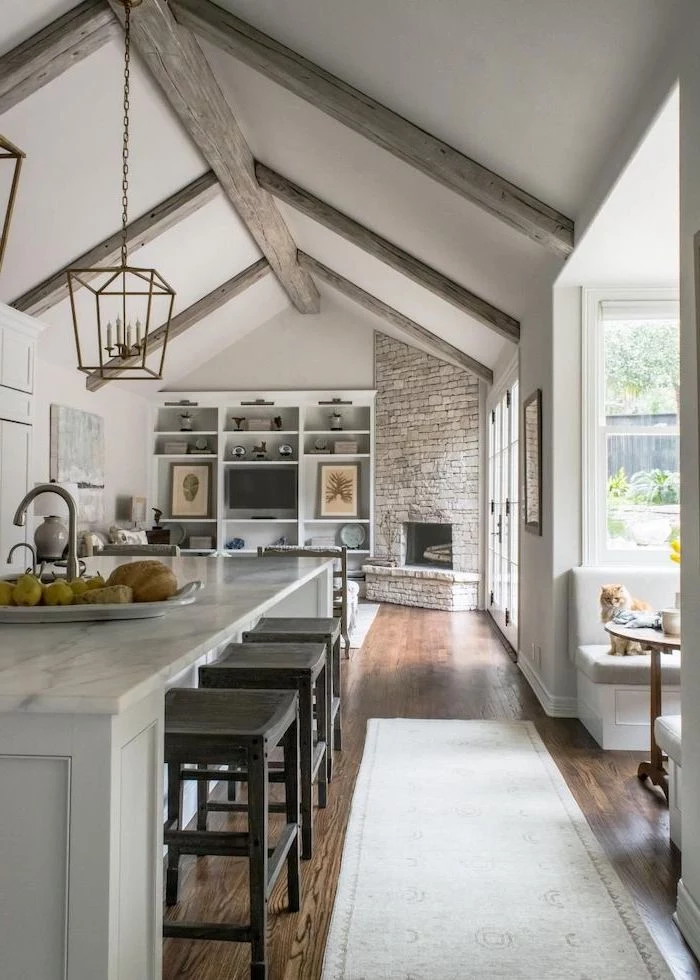 stone fireplace wall, marble kitchen island, what is a vaulted ceiling, wooden floor, grey wooden beams