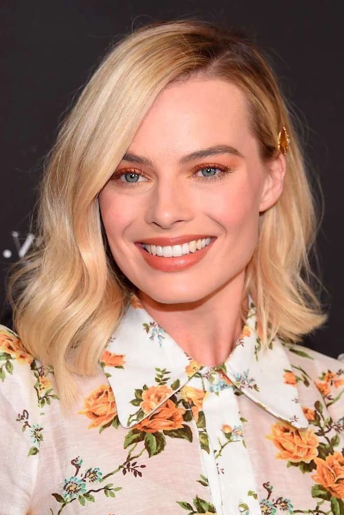margot robbie smiling, blonde wavy hair, side swept, hairstyles for women, wearing white floral shirt