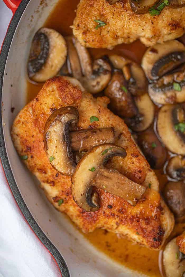 chicken marsala, mushrooms on top, cooked in red skillet, white table, easy dinner recipes for beginners