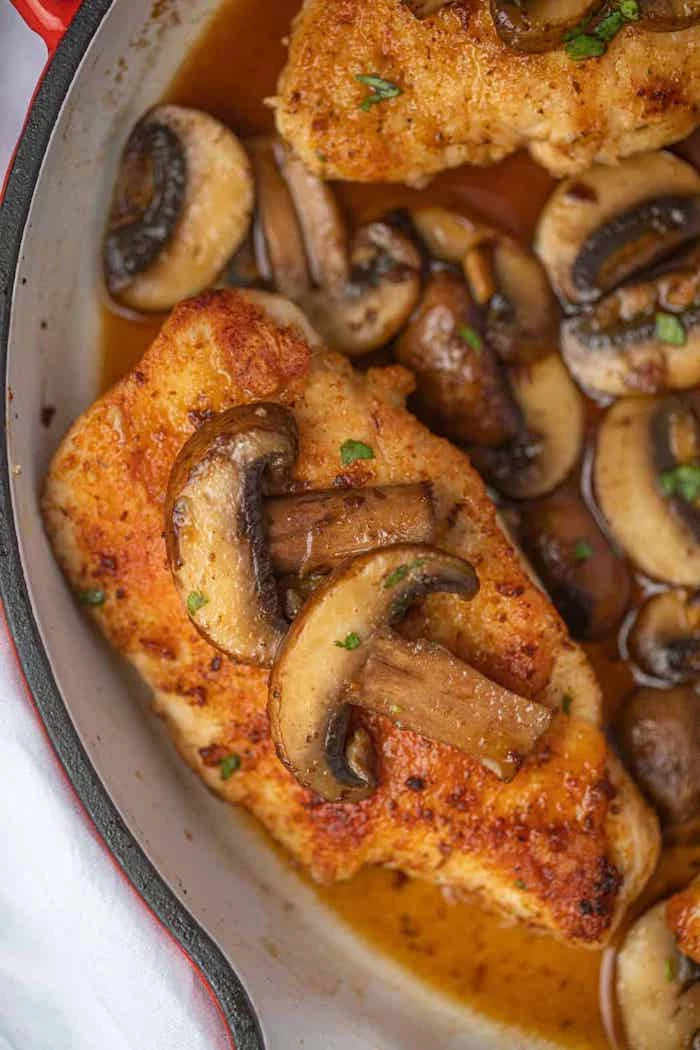 chicken marsala, mushrooms on top, cooked in red skillet, white table, easy dinner recipes for beginners
