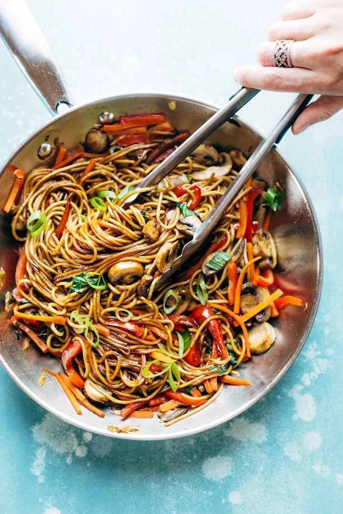 noodles with mushrooms, peppers and onion, cooked in skillet, easy dinner recipes for beginners, with tongs inside