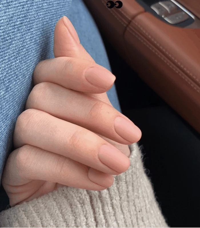 nude nail polish, cute fall nails, hand resting on a leg, white sweater, brown leather, in the background