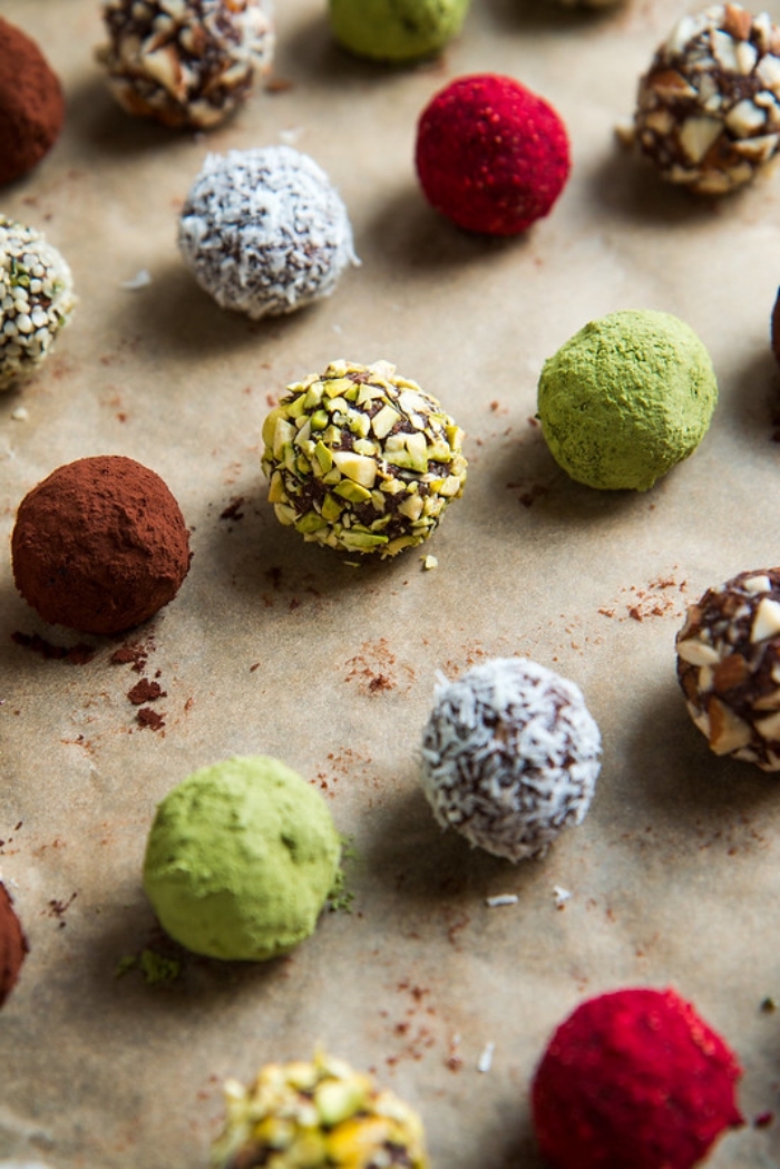 date energy balls, arranged on baking paper, covered with cocoa, coconut flakes, nuts and matcha powder