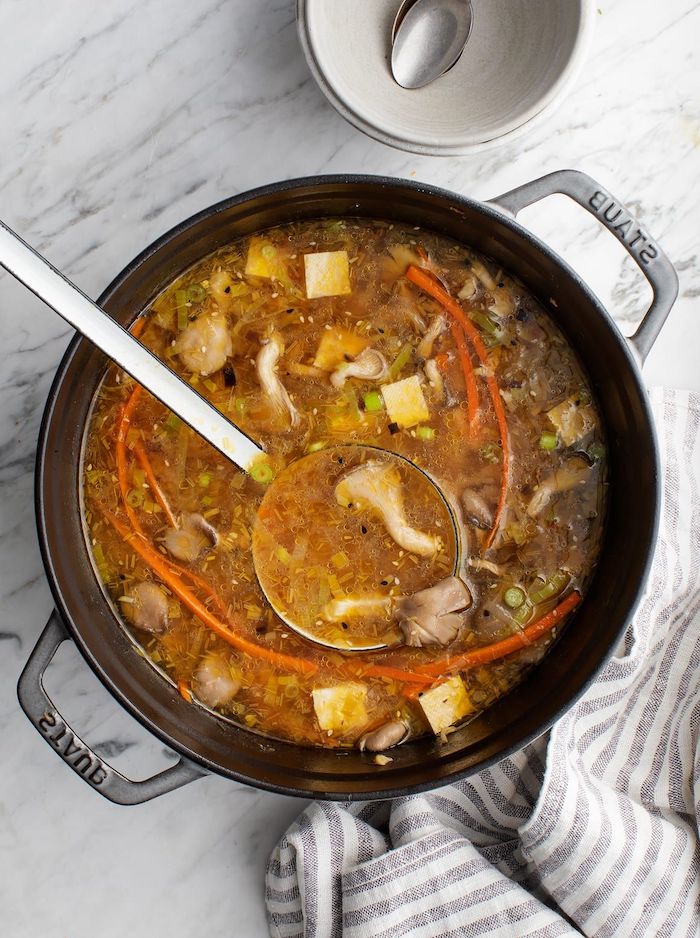 oyster mushrooms soup, in a black pot, healthy dinner ideas, marble countertop, white and grey cloth