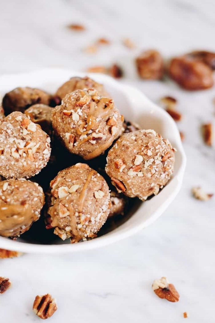 energy bites, with peanut butter drizzle on top, in a white bowl, walnuts scattered around