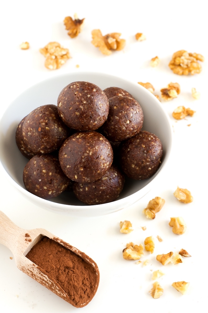 walnuts scattered on white table, cocoa in wooden spoon, protein bites recipe, chocolate truffles, in white bowl