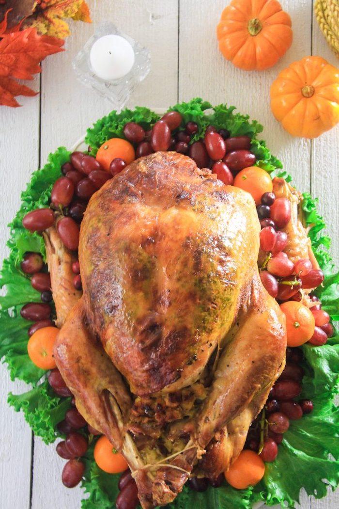 white wooden table, how to prepare a turkey, roasted turkey, on top of green salad, pumpkin decorations