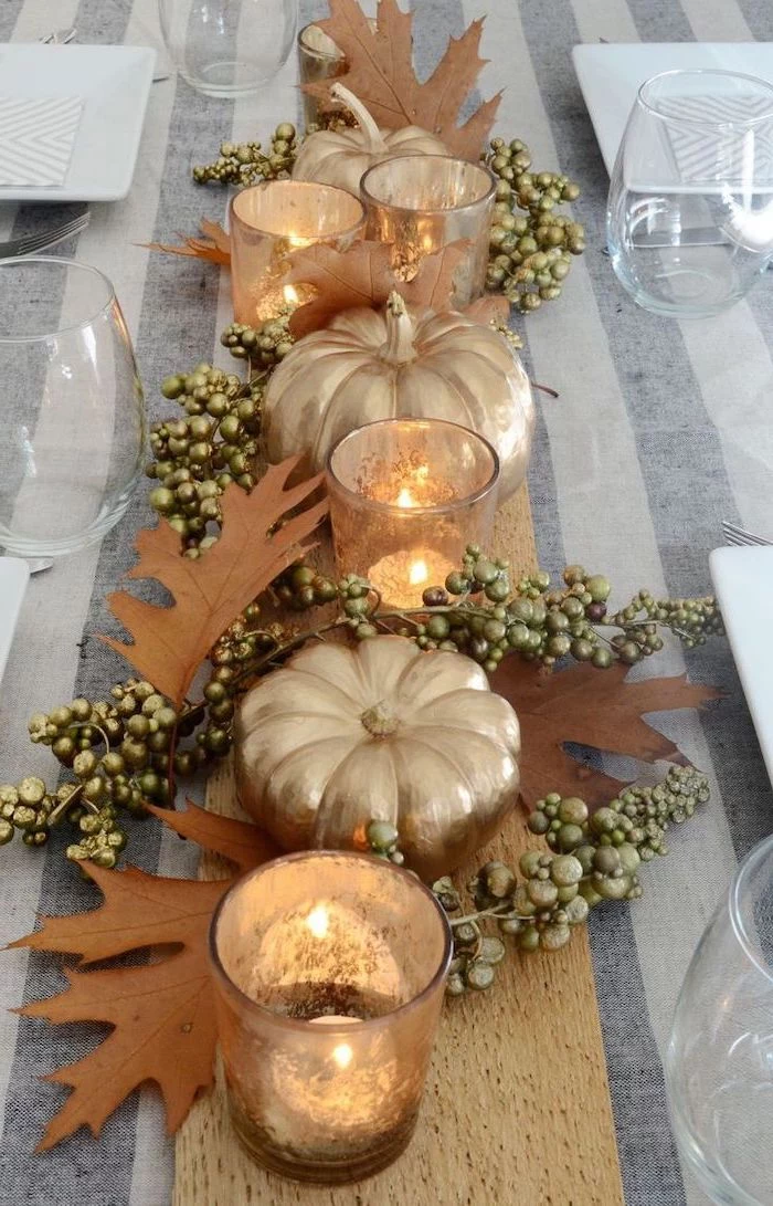 gold pumpkins, fall leaves, candles arranged, in the middle of the table, thanksgiving door decor, water glasses
