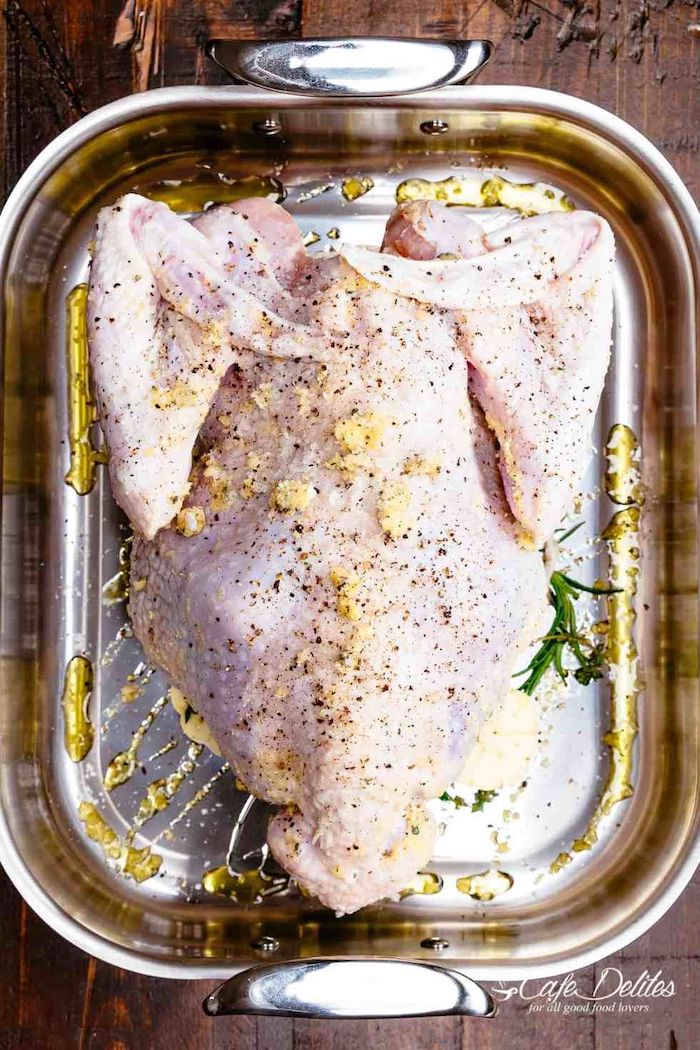 how long to cook a turkey, raw turkey, in a pan, covered in garlic and herbs, wooden table