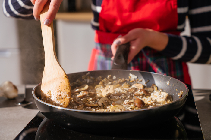 woman stirring rice and mushrooms, in black sauce pan, mushroom risotto recipe, with wooden spoon in hand