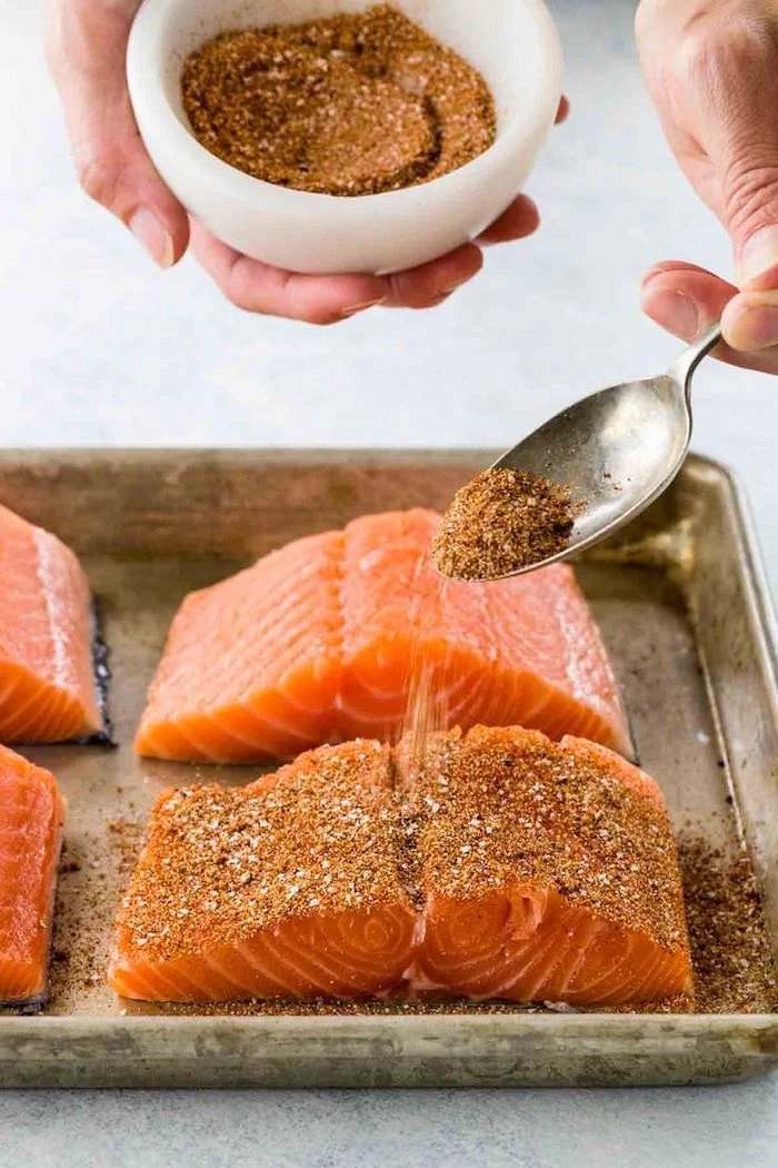 salmon fillet, seasoned with dry herbs, out of a white bowl, with a spoon, low calorie meals, sheet pan