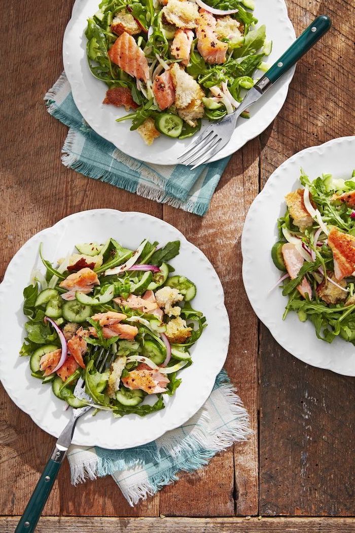 wooden table, healthy dinners for two, white plates, salmon panzanella inside, forks on the side, blue and white table cloths