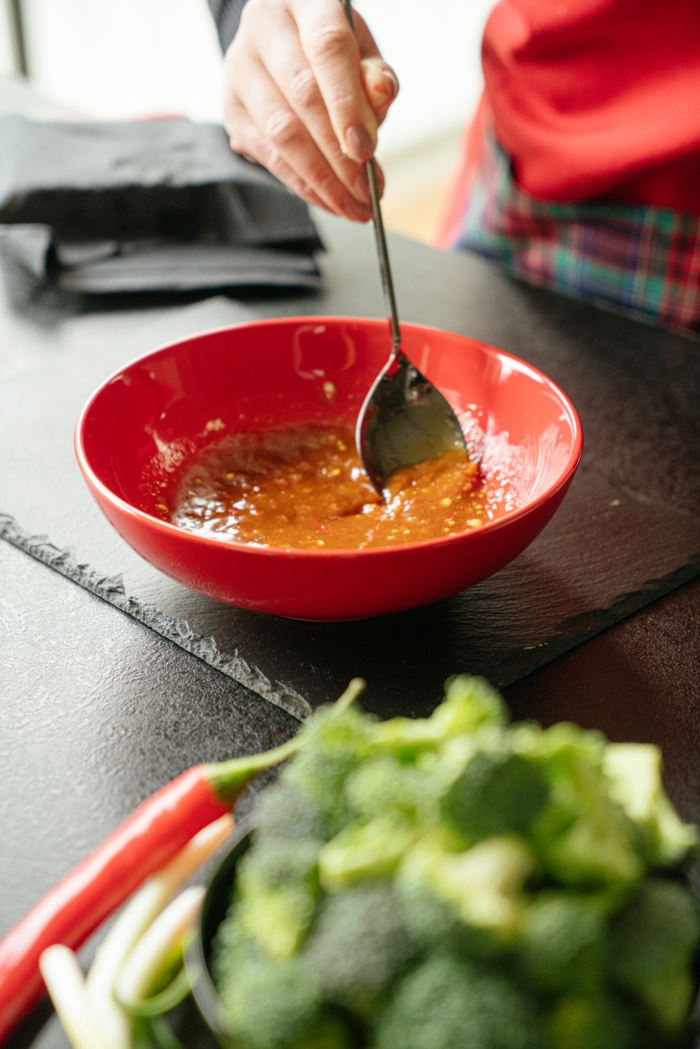 sauce being prepared in red bowl, stirred with metal spoon, asian tofu recipe, placed on black cutting board
