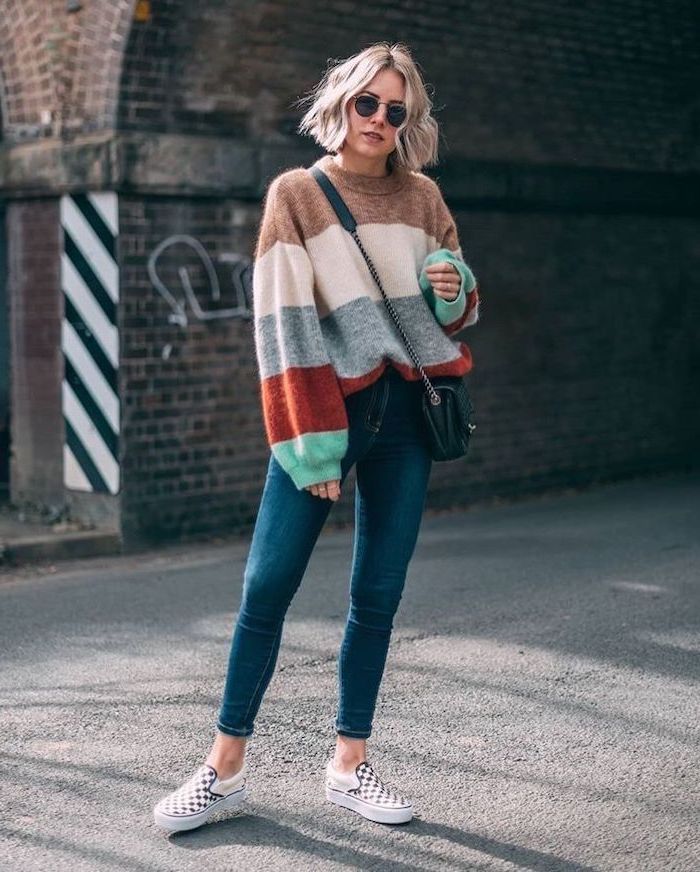 woman standing in the middle of the street, wearing colorful sweater and jeans, layered haircuts with bangs, blonde wavy hair