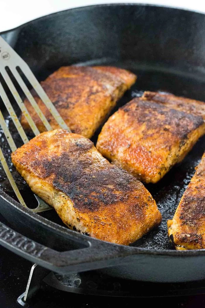 baked salmon, in a black skillet, low calorie meals, metal spatula, white background