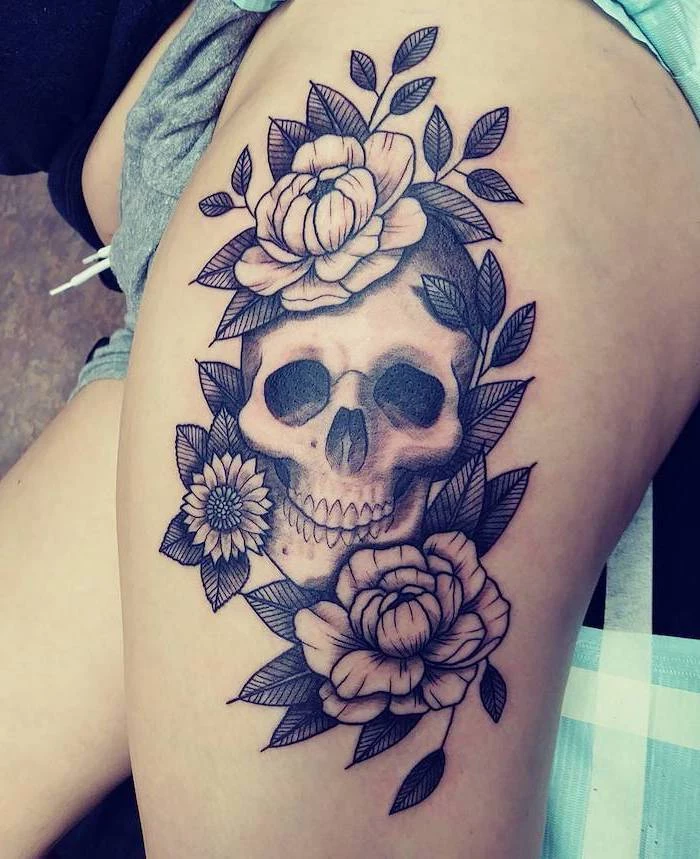 human skull, surrounded by flowers, side thigh tattoo, grey shorts, black t shirt