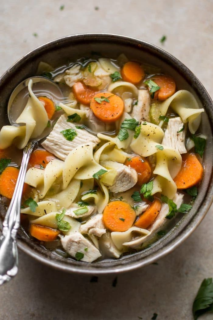 ceramic bowl, turkey noodle soup, chopped carrots, parsley garnish, healthy meal prep, silver spoon
