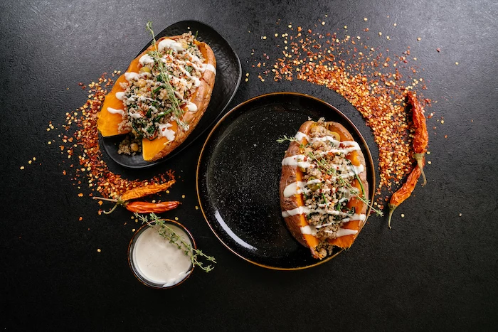easy dinner recipes, stuffed sweet potatoes, with sauce and thyme for garnish, in black plates, on black table, with chili powder on top