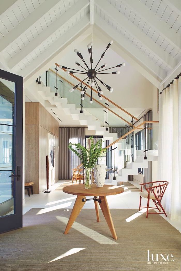 vaulted ceiling kitchen, wooden table, entry door, white staircase, hanging chandelier, white curtains