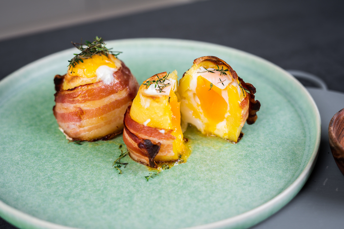 baked potato volcanoes, two potatoes one cut in half, wrapped with bacon, eggs and cheese inside, placed on blue plate