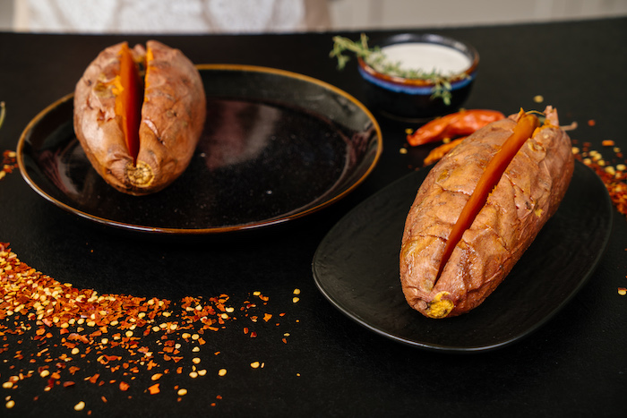 two baked sweet potatoes, sliced in the middle, in black plates, easy dinner recipes, chilli powder, on black table