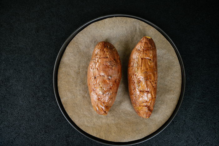 two baked sweet potatoes, easy dinner recipes, on sheet pan, covered with baking paper, on black table