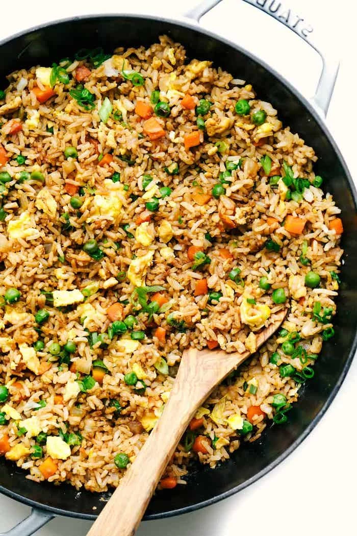rice with vegetables, cooked in a skillet, easy weeknight meals, wooden spoon on the side, white table