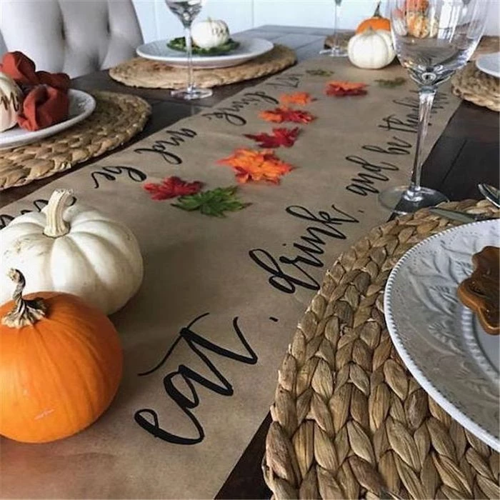 table runner, pumpkins and fall leaves, arranged on it, happy thanksgiving sign, wine glasses, plate settings