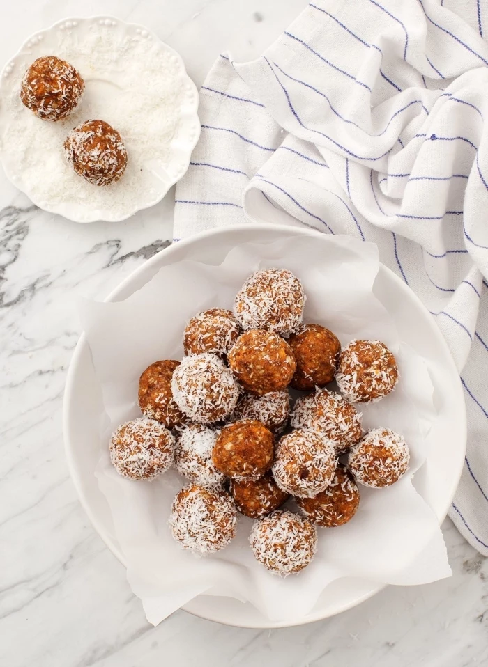  energy balls recipe, covered with coconut flakes, in white plates, white cloth, marble countertop