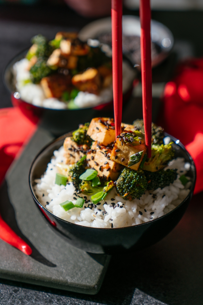 tofu and broccoli on white rice, garnished with black sesame seeds, asian tofu recipe, black bowl and red chopsticks