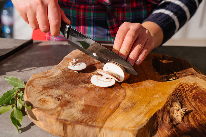 woman cutting up mushroom, on wooden board, placed on grey surface, mushroom risotto recipe, sharp knife