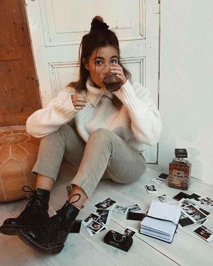 woman sitting on the floor, medium length hairstyles with bangs, wearing white sweater and grey pants, dr martens boots