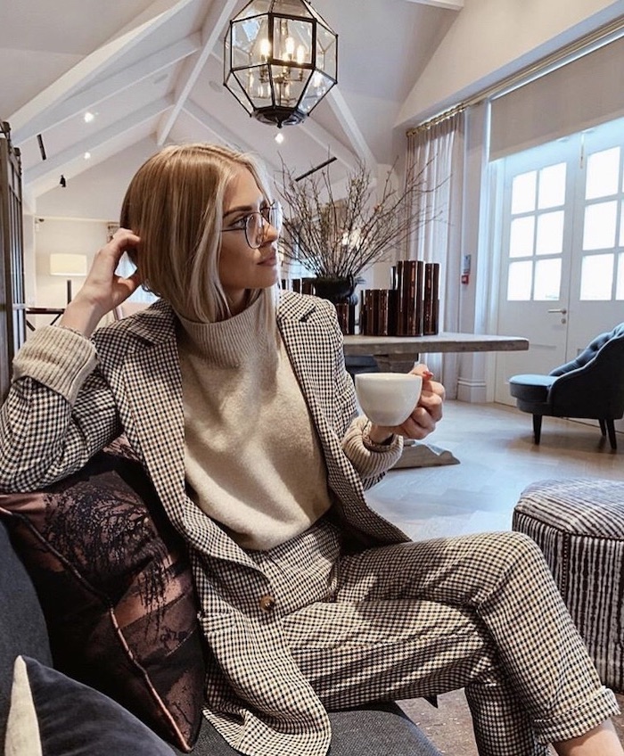 woman sitting on a sofa, wearing a black and white suit, white sweater, short to mid length hairstyles, blonde hair