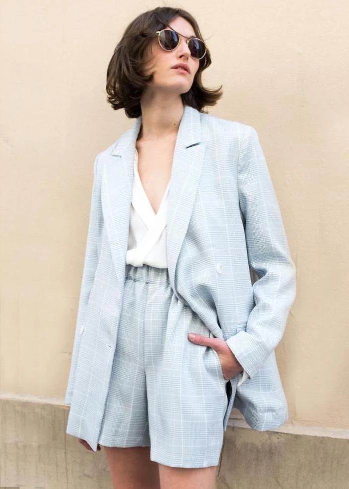 woman leaning on a wall, wearing a blue suit with shorts, white shirt, short to mid length hairstyles, black hair