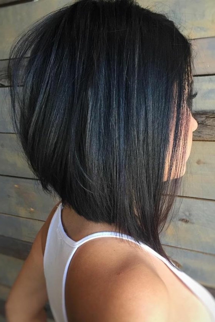 collarbone length hair, woman wearing white top, asymmetrical black hair, wooden wall in the background