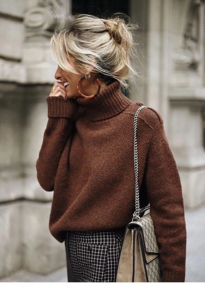 woman smiling, walking down the street, wearing brown sweater, blonde hair in a messy bun, collarbone length hair