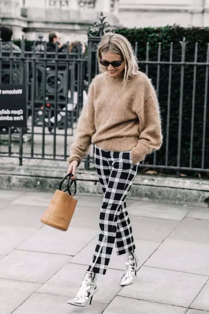 woman walking down the street, wearing beige sweater, black and white pants, silver boots, collarbone length hair, blonde hair