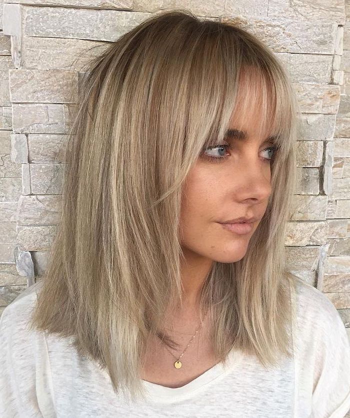 woman leaning on a white brick wall, medium hairstyles 2019, wearing white blouse, blonde hair with bangs