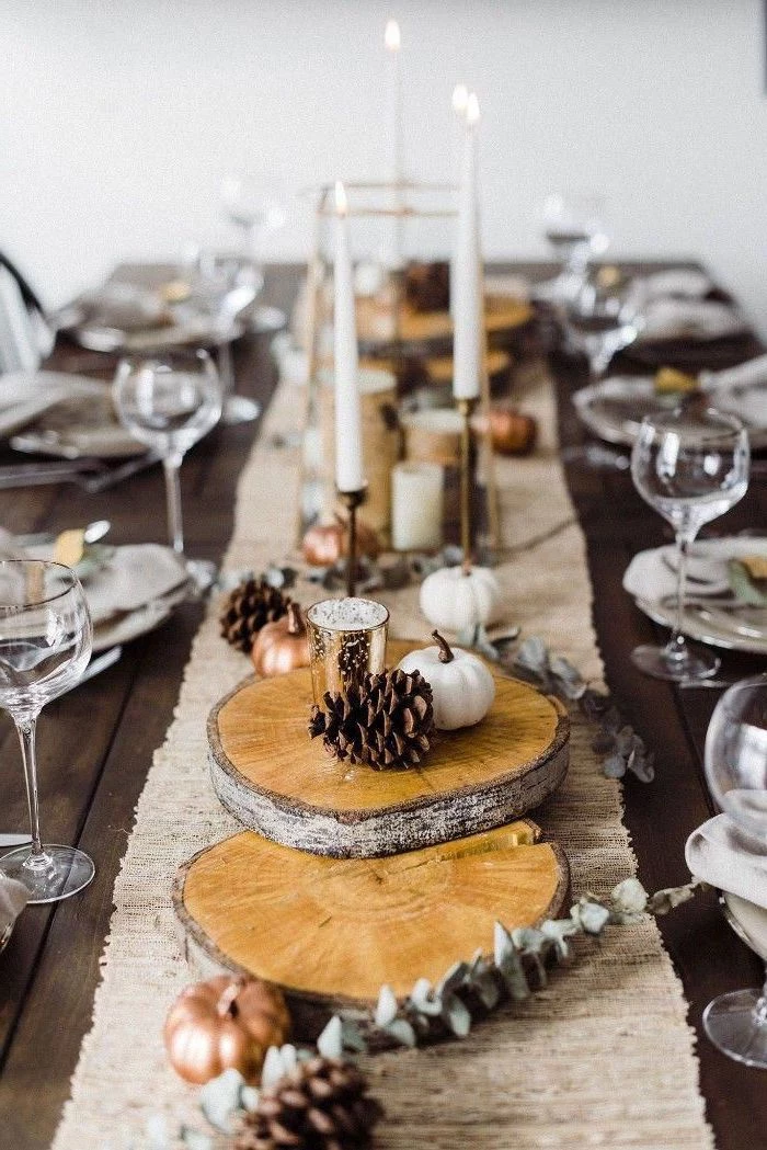 wooden logs, pine cones, pumpkins and candles on them, happy thanksgiving sign, table runner, wine glasses