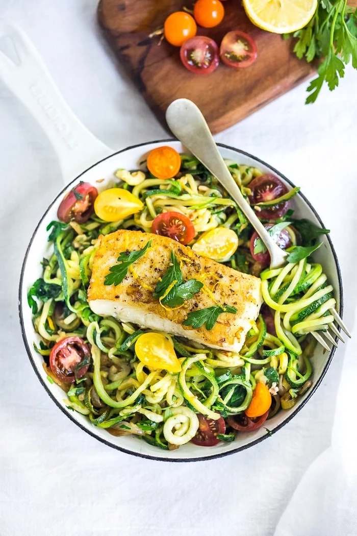 zucchini noodles, cherry tomatoes, fish fillet, foods to avoid to lose weight, white bowl, white table