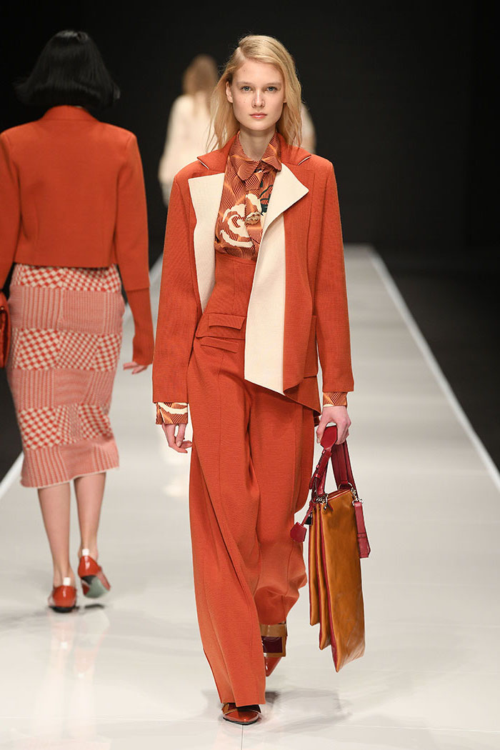 model walking down the runway, current fashion trends, wearing all orange suit, consisting of pants blouse and blazer