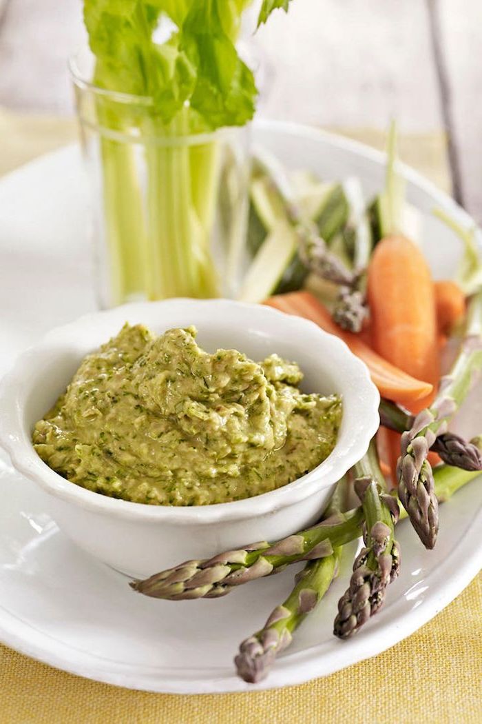 artichoke dip in small white bowl, on white plate, easy party snacks, carrots and artichoke on the side