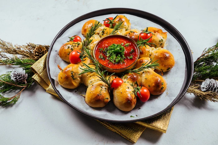 pull apart christmas bread, rosemary branches and halved cherry tomatoes on it, tomato salsa in a bowl in the middle
