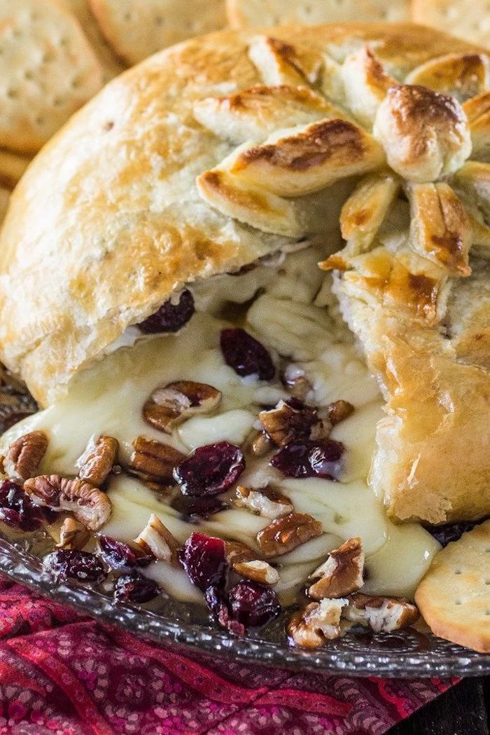 baked dough with brie cheese inside, dried cranberries and chopped walnuts, finger foods for party, crackers on the side