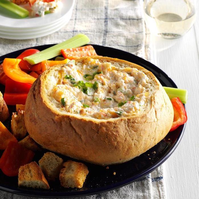 crab dip inside a hollowed bread, best appetizer to bring to a party, placed on black plate, vegetable sides on the side