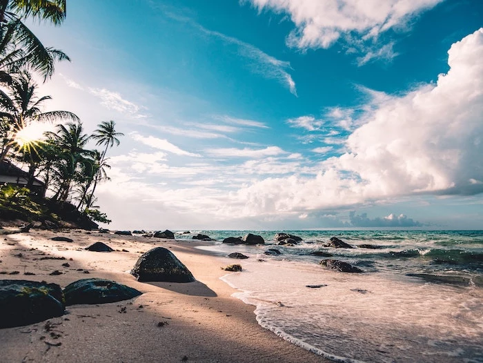 beach with palm trees and rocks at sunset, white clouds in the sky, turquoise clear water waves, beautiful beaches